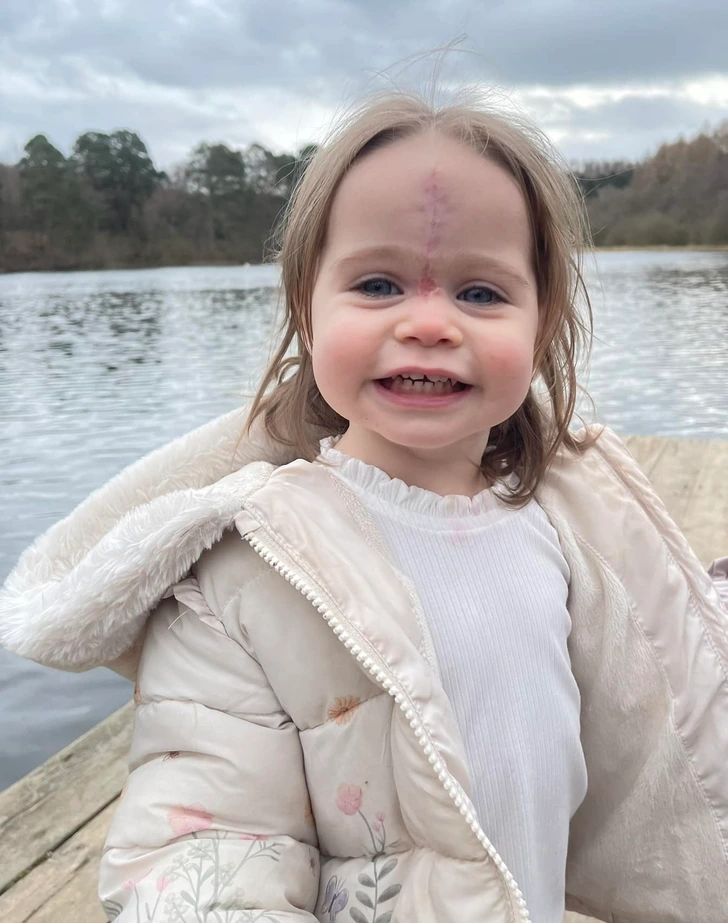 Little girl smiling in front of a large body of water and trees. 
